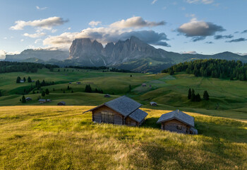 Obraz premium Aerial view of Seiser Alm valley with traditional wooden mountain huts in Dolomites Italy . Morning drone shot of idyllic Alpe di Suisi blooming meadow in South Tyrol 
