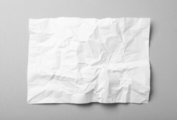 Sheet of white crumpled paper on grey background, top view