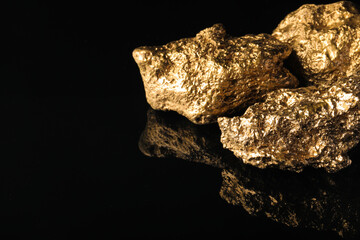 Obraz premium Gold nuggets on black reflective surface, space for text