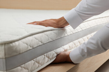 Man touching soft white mattress indoors, closeup