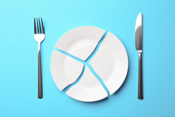 Pieces of broken ceramic plate and cutlery on light blue background, flat lay