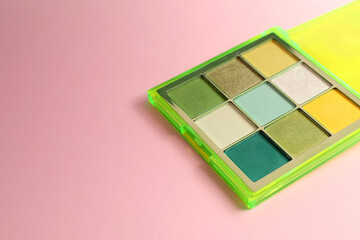Colorful eyeshadow palette on light pink background. Space for text
