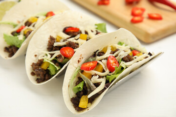 Delicious tacos with fried meat, vegetables and cheese on white wooden table, closeup