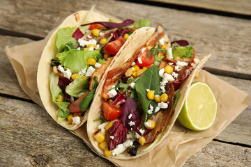 Delicious tacos with fried bacon and lime on wooden table, closeup