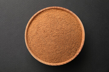 Wooden bowl with aromatic cinnamon powder on grey background