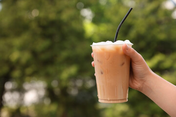 Woman holding plastic takeaway cup of delicious iced coffee outdoors, closeup. Space for text