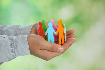 Man holding paper human figures on blurred background, closeup. Diversity and Inclusion concept