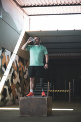 A middle-aged athlete with a bionic leg drinking water while standing on a box.