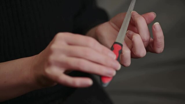 A woman straightens her nails with a nail file. Female nails and nail file. Alignment of the edge of the nail. Manicure at home for yourself.