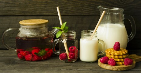 Glass cups with hot and cold drinks on a wooden background.  Jug with fresh milk and glass teapot with raspberry tea.  Homemade, fresh, fragrant cookies.  Rustic style concept, body products. 