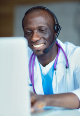 Portrait of young male doctor wearing headset while using computer at desk in clinic. Doctor.