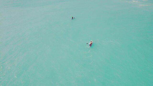 Aerial view of family supboarding on sandy beach. Mom and dad oaring on paddleboards with their sons down azure sea