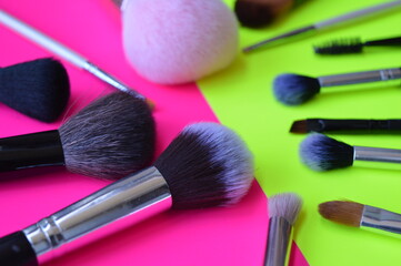 Professional cosmetic makeup brushes of different sizes on a pink and green background for applying powder, shadows and blush and other cosmetic products