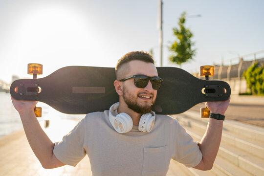Young smiling man holding skateboard walking on the street.