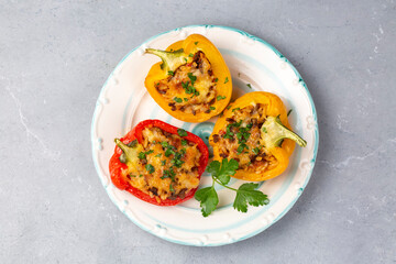 Stuffed peppers, halves of peppers stuffed with rice, dried tomatoes, herbs and cheese in a baking dish on a blue wooden table, top view. (Turkish name; biber dolmasi)