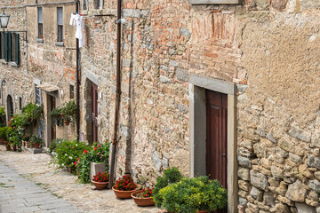 Picturesque ancient light stone buildings with lots of flower pots beside doors and building wall. 