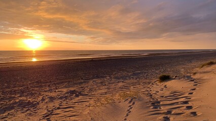 Schönes orangefarbenes Licht bei Sonnenuntergang an einem Strand an der Nordsee in Dänemark mit Fußspuren in Richtung Ozean