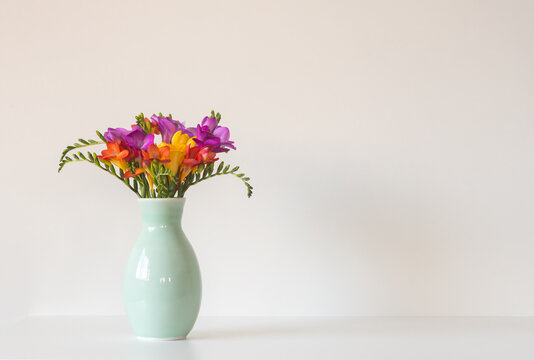 Close up of colourful freesia flowers in green vase against white background with copy space to right (selective focus)