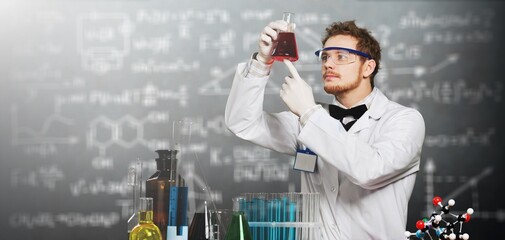 A young chemist conducting experiment mixing liquids in flask, laboratory assistant showing chemical reaction, science concept, blackboard background
