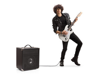 Full length portrait of a young musician playing a guitar plugged into an amplifier - obrazy, fototapety, plakaty