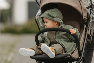 A female toddler is sitting in the stroller on a cloudy day. A young girl in a baby carriage in a village green.