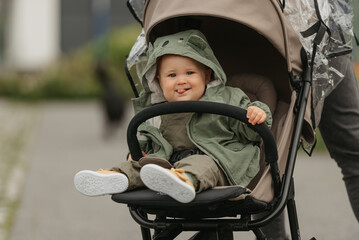 A female toddler with tongue out is sitting in the stroller on a cloudy day. A young girl in a baby carriage in a village green.