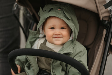 A close photo of a female toddler who is sitting in the stroller on a cloudy day. A young girl in a baby carriage in a village green.