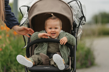 A female toddler is chilling in the stroller on a cloudy day. In a green village, a young pretty girl in a raincoat is singing in her baby carriage.