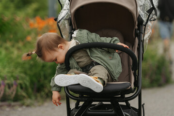 A female toddler is chilling in the stroller on a cloudy day. In a green village, a young pretty...