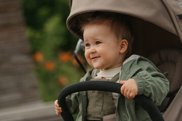 A close portrait of a female toddler who is holding the safety bumper bar of the stroller on a...