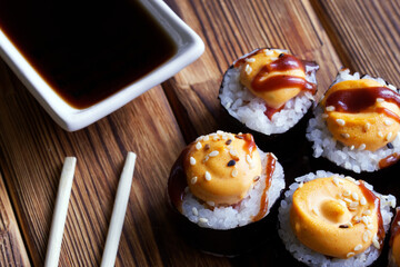 Appetizing rolls with rice, nori, fish and spices, sticks - varibashi and gravy boat - seyuzaru on a table made of natural pine boards. Macro. Selective focus.