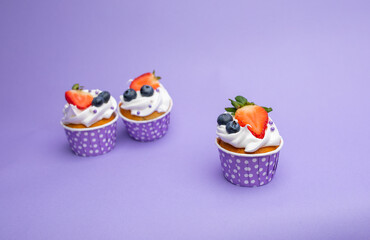  Beautiful photo of three delicious cupcake, desert with strawberries and blueberries in a lilac stand with white polka dots, on a purple background