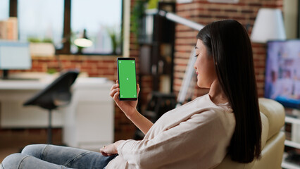 Young adult person sitting on couch with mobile cellphone having mockup chroma key background....