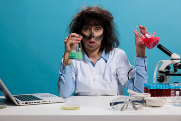 Mad silly looking crazy lab worker sitting at desk while having glass jars filled with experimental...