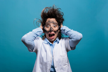 Psycho and scared mad chemist screaming in panic after dangerous chemical explosion and failed scientific experiment. Weirdo scientist with messy hair and dirty face shouting on blue background. - obrazy, fototapety, plakaty