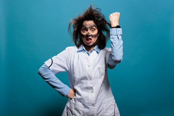 Crazy scientist with dirty face and wacky hair angrily clenching and raising fist in air while...