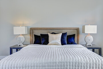 Bed with blue and white bedding and natural luxury tones lamps, wall and bed frame. Design details. 