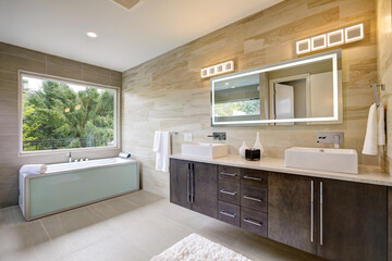 Contemporary bathroom interior with beige ceramic tiles, luxury details, huge light up mirror and two sinks. 
