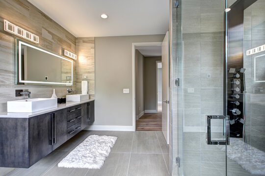 Contemporary bathroom interior with beige ceramic tiles, luxury details, huge light up mirror and two sinks. 