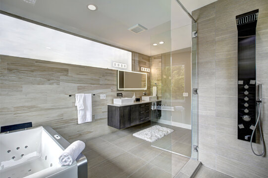 Contemporary luxury  bathroom interior with beige ceramic tiles and hot tub without shower curtain. Standing in the shower with large glass door. 