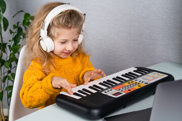 a little blonde girl in headphones smiling and playing the synthesizer, the concept of teaching children music