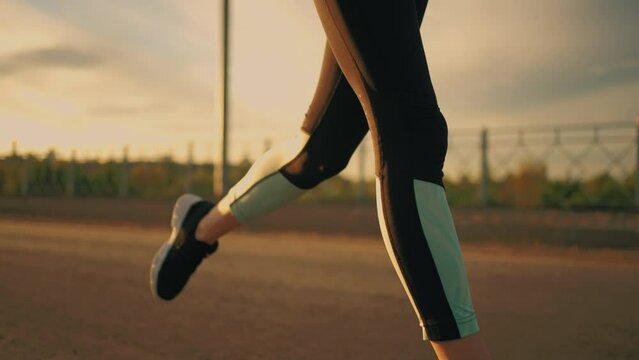 athletic woman is running outside in sunset or evening, close up of body dressed in sportswear