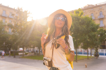 A tourist with a travel hat in the sunset, with a photo camera in the city