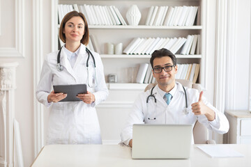 Portrait photo of two young smiling doctors in white medical gown in the clinic office. Colleagues meeting, discussion and health care concept