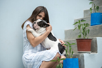 Young latin woman caresses and hugs her dog (french bulldog) next to the stairs