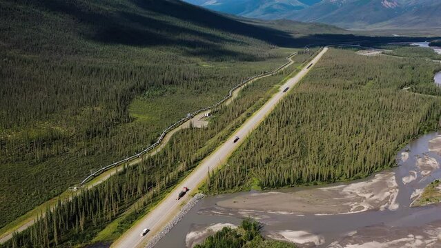 Aerial tilt up on Alaska Brooks Range Mountain Portage Valley with Tank Trucks driving Portage Glacier road and Trans Alaska crude oil Pipeline 