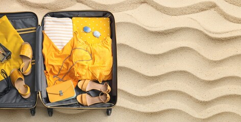 Open suitcase with beach accessories on sand, top view. Travel concept