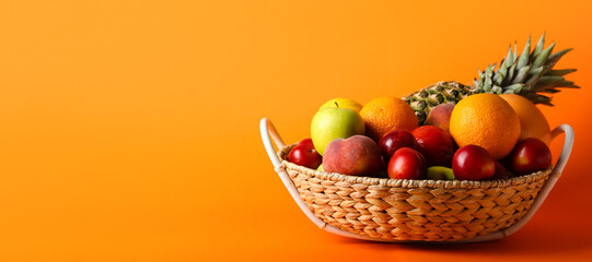 Basket with fresh fruits on orange background with space for text
