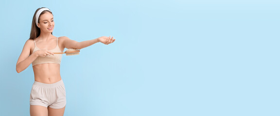 Fototapeta premium Beautiful young woman with massage brush on light blue background with space for text