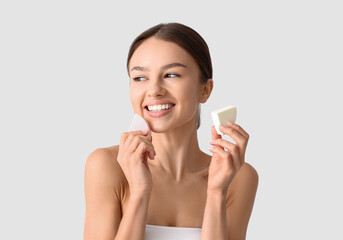 Pretty young woman with makeup sponges on grey background